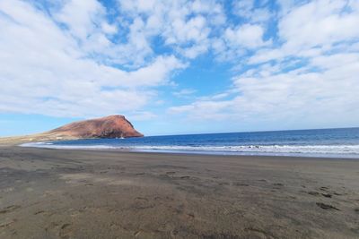 La tejita ocean beach with red rock formation on the horizon blue sky and fluffy white cloude 