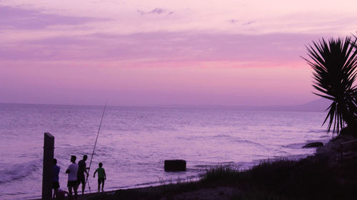 Silhouette people on beach against sky during sunset