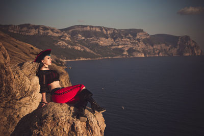 Woman sitting on rock by mountain against sky