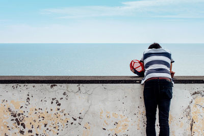 Rear view of person standing at retaining wall by sea against sky