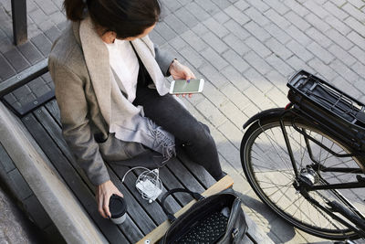 High angle view of woman surfing net through mobile phone while sitting on bench in city