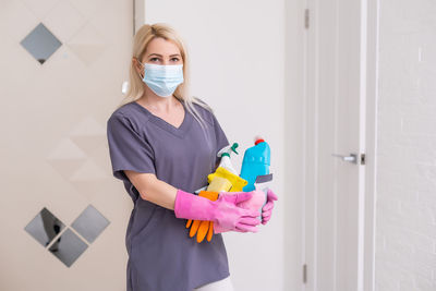 Portrait of woman wearing mask holding cleaning equipment