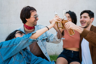 Friends toasting beer bottle against wall