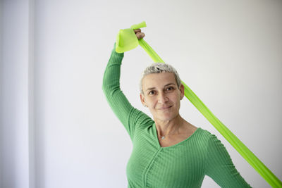 Portrait of young woman with arms raised standing against wall