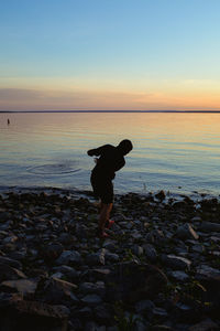 Man standing on rocks at beach during sunset