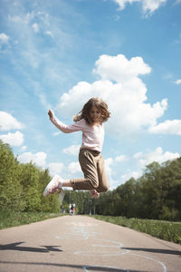 Rear view of woman jumping on road against sky