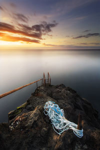 Rope on rock formation at sea against sky during sunset