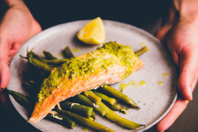 Close-up of hand holding fish and green beans in plate