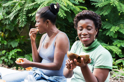  young woman picnic with her girlfriend sitting on the ground is currently sharing a lawyer fruit