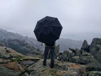 Man with umbrella on a mountain peak with his back to the camera 