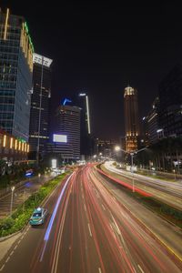 Light trails on road amidst buildings against sky at night