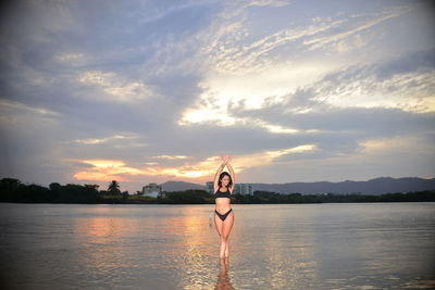 Silhouette woman standing by lake against sky during sunset