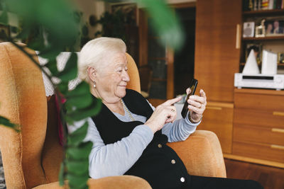 Senior woman sitting in the living room using smartphone