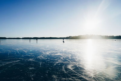 People ice-skating on frozen lake against sky on sunny day