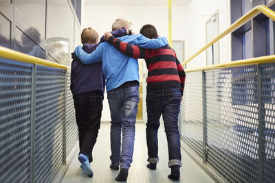 Full length rear view of boys walking arm around in school corridor