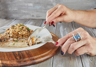 Hands of a woman with manicure and ring with diamonds and blue topaz eating fillet of white fish