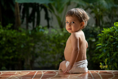 Side view of shirtless boy standing against trees