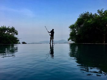 Man fishing in lake against sky