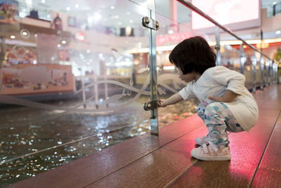 Girl holding glass knob while crouching in shopping mall