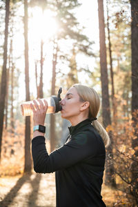 A woman in a black suit in the park drinks water with sports nutrition for outdoor training