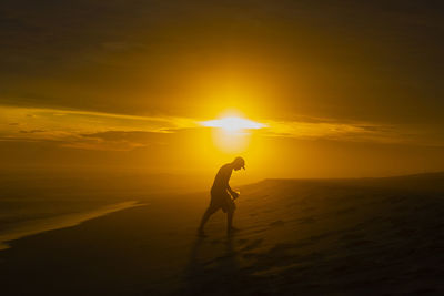 Silhouette woman standing on beach against sky during sunset