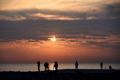 Silhouette people on beach against sky during sunset