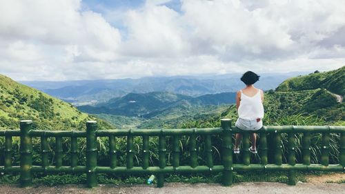 Rear view of woman sitting on railing against sky