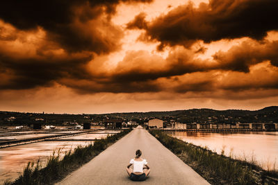 View of road by canal against sky during sunset