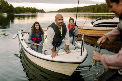 Family looking at woman anchoring boat near pier during sunset