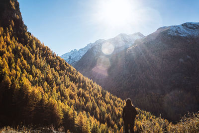 Rear view of woman standing on mountain against sky during sunny day