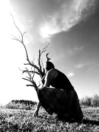 Low angle view of woman sitting on field against sky