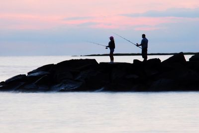 Silhouette men fishing on beach against sky during sunset