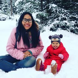 Portrait of smiling mother and daughter sitting on snow covered land during winter