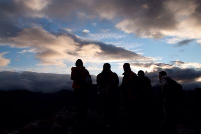 Silhouette friends on mountain top against cloudy sky