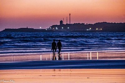 Rear view of men on beach against sky during sunset