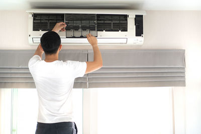 Rear view of man repairing air conditioner at home