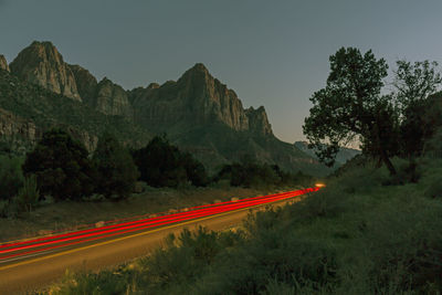 Light trails on road by mountain against sky