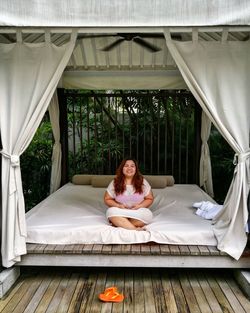 Portrait of smiling woman sitting on outdoor bed at luxury hotel