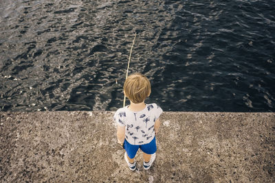 High angle view of boy standing on pier fishing in sea