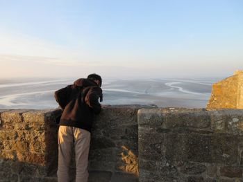 Man photographing on wall against sea and sky