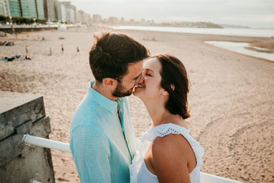 Full length of couple embracing while standing on beach against sky