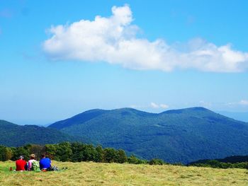 Rear view of people sitting on landscape against blue sky