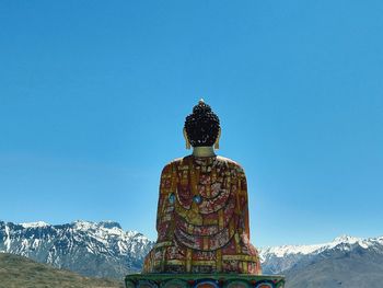 Buddha statue against snowcapped mountains and clear sky