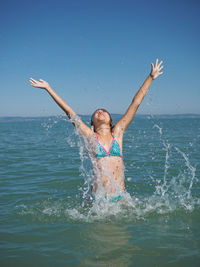 Girl splashing water in sea against clear sky