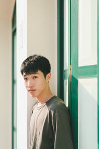 Portrait of young man standing against window