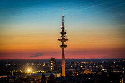 Illuminated buildings in city against sky during sunset