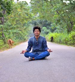 Man doing yoga on road against trees