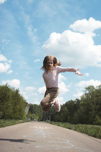 Rear view of woman jumping on road against sky