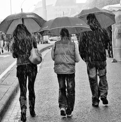 Rear view of people walking with umbrella on footpath during rain