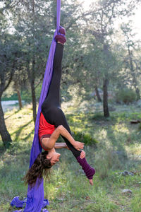 Young girl acrobat. practicing aerial silks. woman doing circus stunts with clothes in the forest. footlock invert stretching. warn up before play.